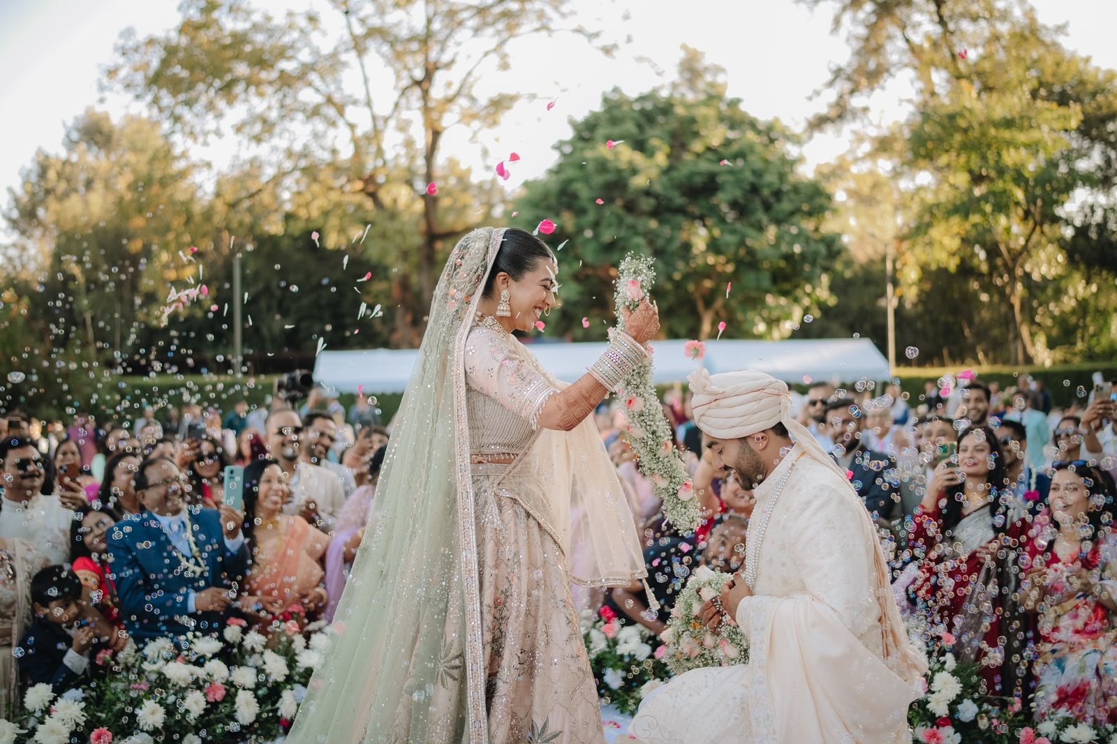Ankshita lifting the garland over Rohit as guests throw petals and bubbles