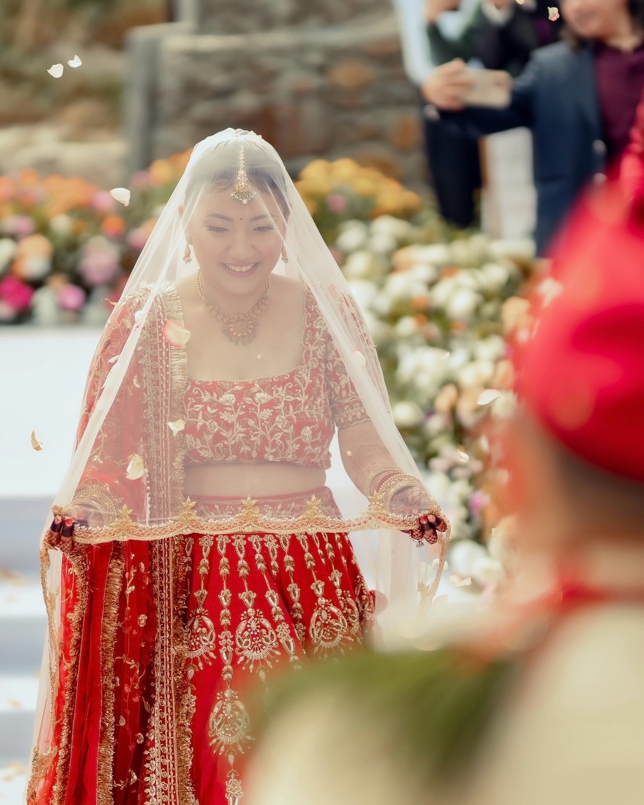 Kusum under a sheer veil, smiling as petals fall around her