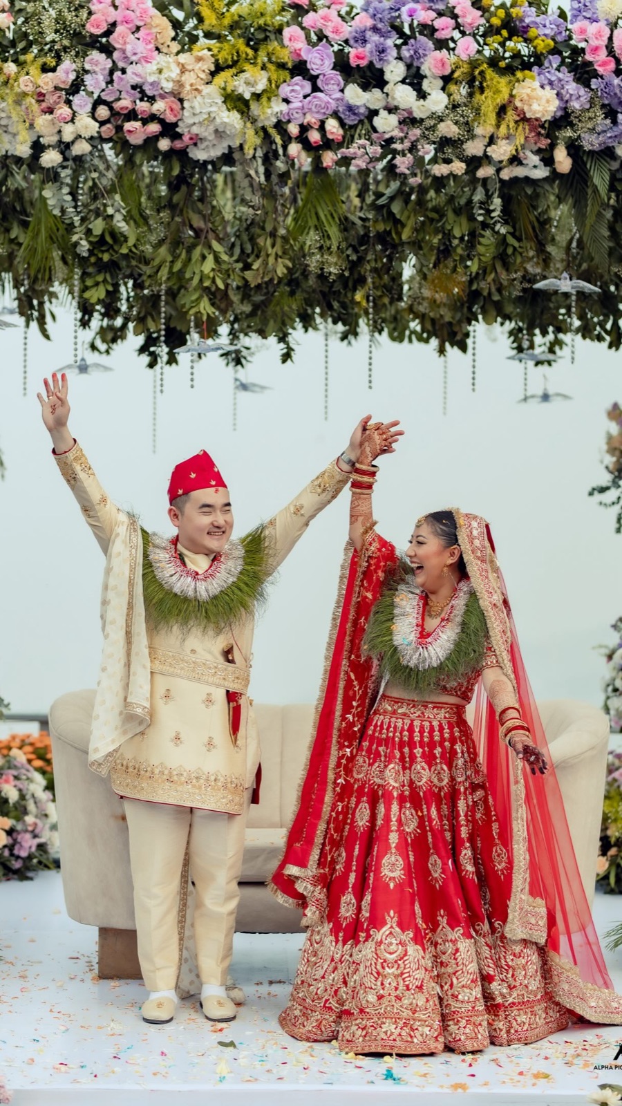 Kusum and her husband raising their joined hands under a canopy of flowers