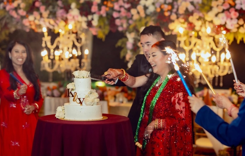Kusum and her husband cutting a white cake as guests hold up sparklers