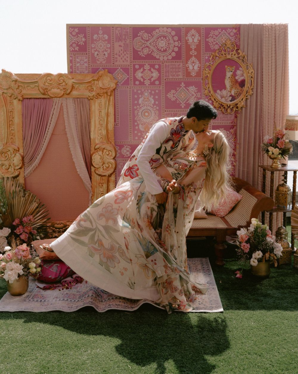 Karan dipping Natalia for a kiss in front of a pink backdrop and gilded frames