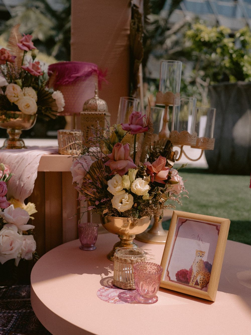 Peach roses in a gold vase beside a framed picture on a peach table