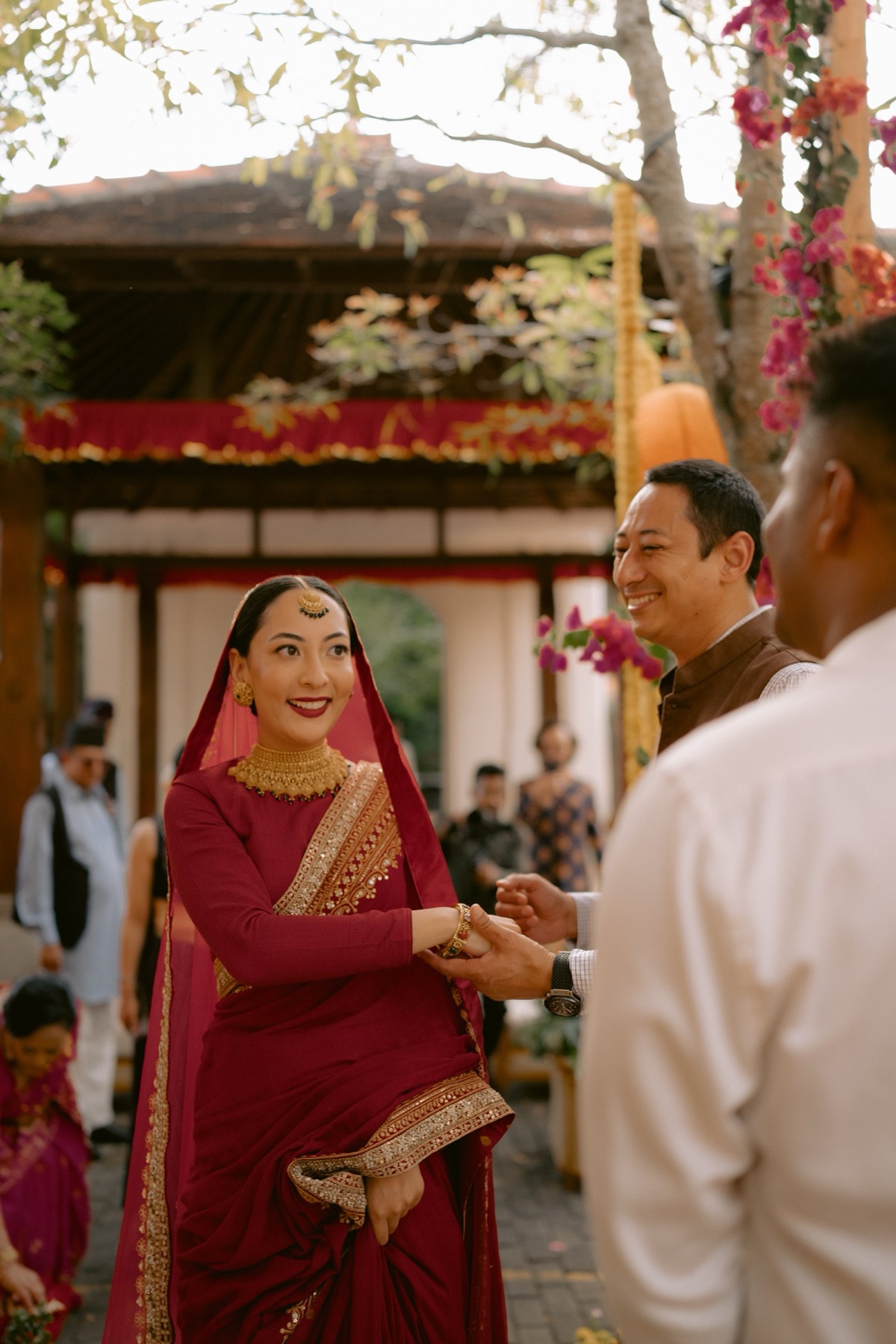 Shaibyaa in a red and gold sari at her wedding, smiling as she greets a guest