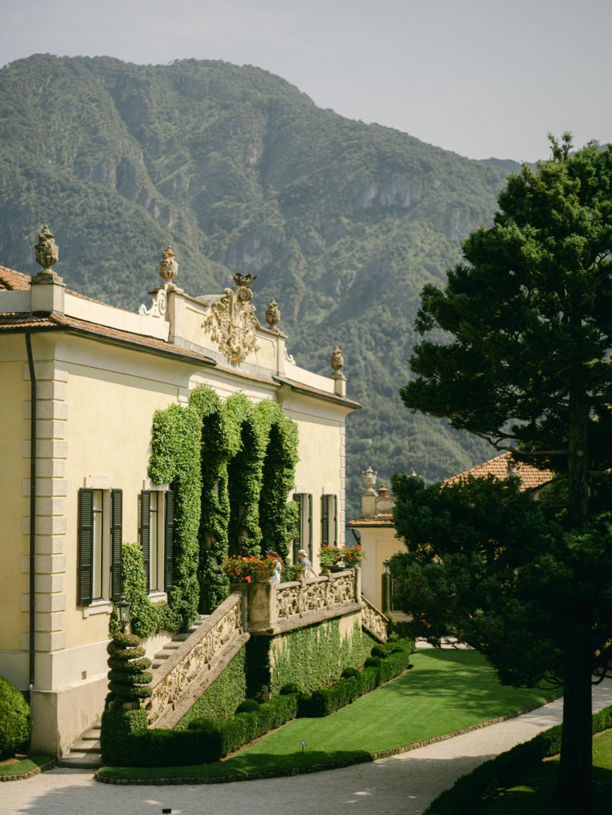 A pale villa with climbing ivy on its steps, mountains behind