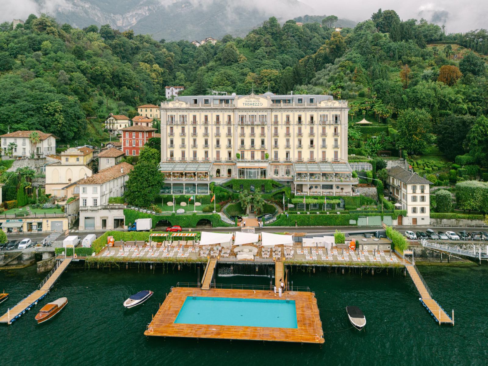 A grand lakeside hotel with a floating pool and boats on the water